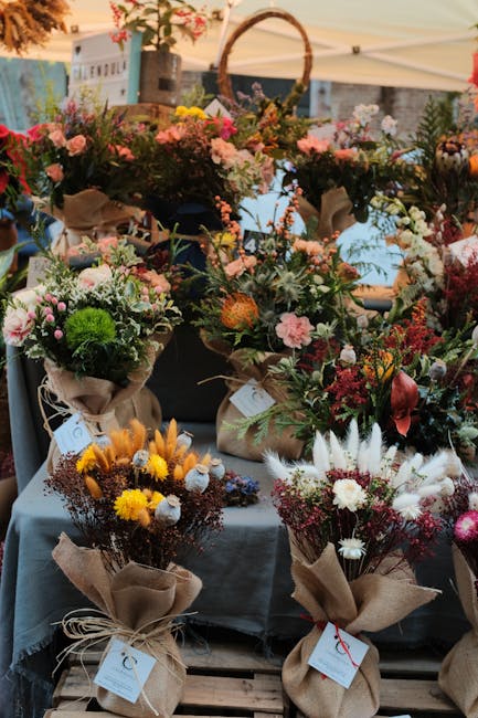 A vibrant display of various floral arrangements at an outdoor market stall, featuring bouquets composed of roses, daisies, chrysanthemums, and other mixed seasonal flowers in shades of pink, yellow, 